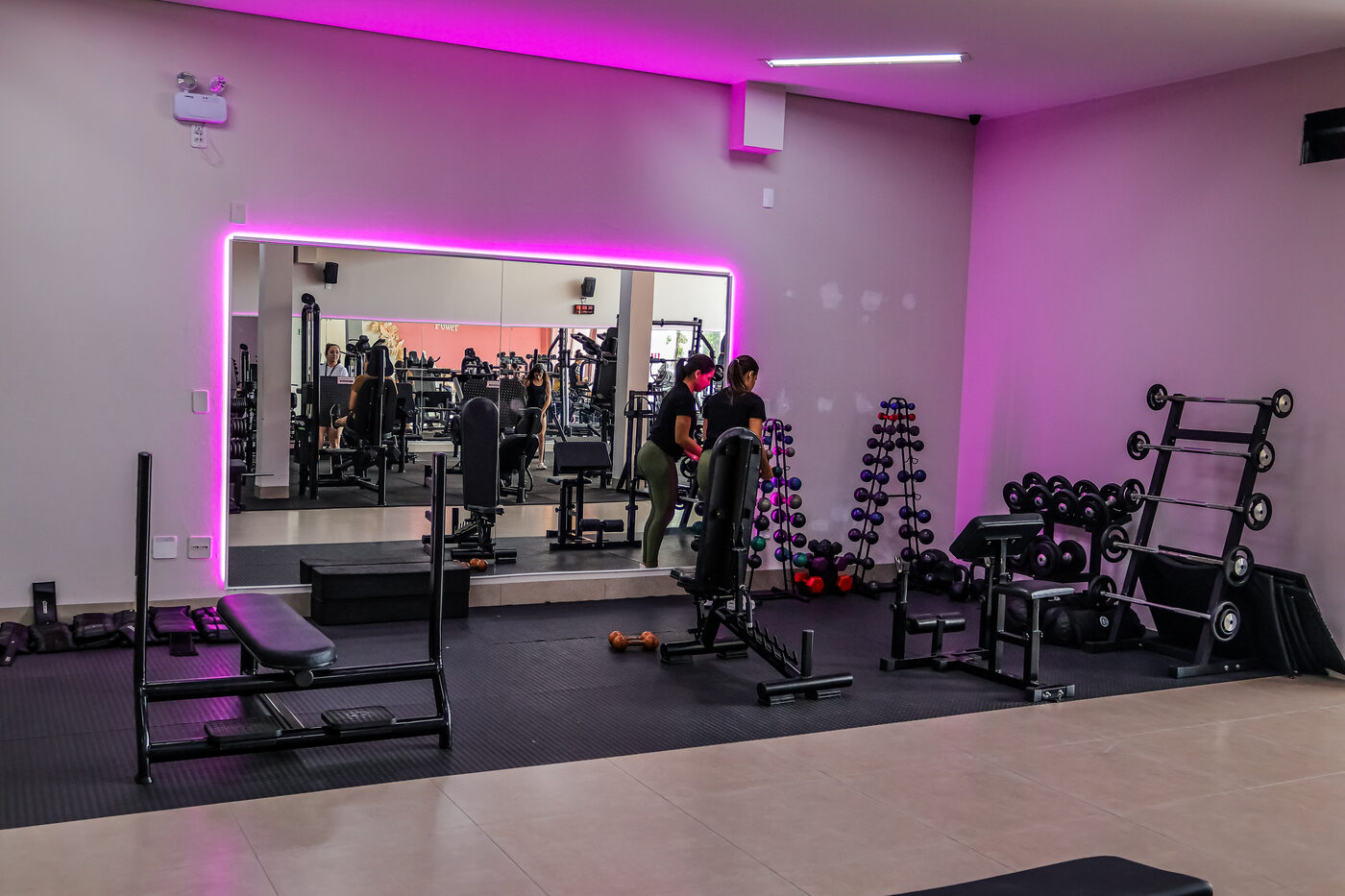 Personal trainer acompanhando aluna na área de pesos livres